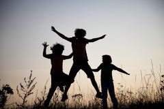 Kinder, die das Springen auf die Sommersonnenuntergangwiese silhouettiert spielen lizenzfreies stockfoto Kinder, die das Springen auf die Sommersonnenuntergangwiese silhouettiert spielen lizenzfreies stockfoto