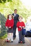 Kinder, die Roller auf ihren Schulweg mit Vater reiten lizenzfreies stockbild Kinder, die Roller auf ihren Schulweg mit Vater reiten lizenzfreies stockbild