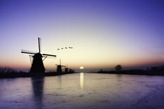 Kinderdijk - gansos que vuelan sobre salida del sol en la alineación congelada de los molinoes de viento fotografía de archivo libre de regalías Kinderdijk - gansos que vuelan sobre salida del sol en la alineación congelada de los molinoes de viento fotografía de archivo libre de regalías