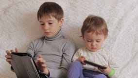 Kinderen die op laag het spelen op uw tablet en telefoon zitten stock video Kinderen die op laag het spelen op uw tablet en telefoon zitten stock video