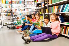 Kinderen die op vloer in bibliotheek en het bestuderen zitten stock foto's Kinderen die op vloer in bibliotheek en het bestuderen zitten stock foto's