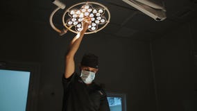 Kirurgi-, medicin- och folkbegrepp - kirurg i maskering som justerar lampan i fungeringsrum på sjukhuset arkivfilmer Kirurgi-, medicin- och folkbegrepp - kirurg i maskering som justerar lampan i fungeringsrum på sjukhuset arkivfilmer