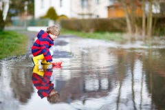 Kleinkindjunge, der mit Papierboot durch Pfütze spielt lizenzfreie stockfotografie Kleinkindjunge, der mit Papierboot durch Pfütze spielt lizenzfreie stockfotografie