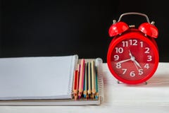 Kleurpotloden en notitieboekjes op een lijst met de wekker De levering van de school en van het bureau Front View stock fotografie Kleurpotloden en notitieboekjes op een lijst met de wekker De levering van de school en van het bureau Front View stock fotografie