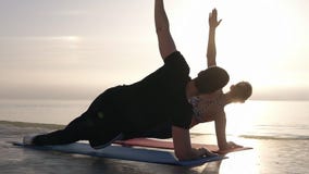 Knap, geschikt jong paar die wat yoga vooraan uitoefenen het overzees en een zijplank samen doen Kaukasisch paar stock video Knap, geschikt jong paar die wat yoga vooraan uitoefenen het overzees en een zijplank samen doen Kaukasisch paar stock video