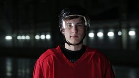 Knappe hockeyspeler Glimlachend bij camera op donkere arena, sluit omhoog portret van verdediger of door:sturen Canadese speler stock videobeelden Knappe hockeyspeler Glimlachend bij camera op donkere arena, sluit omhoog portret van verdediger of door:sturen Canadese speler stock videobeelden