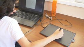 Knappe moderne jongenstiener die aan een grafische tablet werken Hij bekijkt het laptop scherm 4k, langzame motie stock footage Knappe moderne jongenstiener die aan een grafische tablet werken Hij bekijkt het laptop scherm 4k, langzame motie stock footage