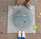Female and Men legs standing in front of a beautifully decorated Manhole of Kobe City, Japan stock image Female and Men legs standing in front of a beautifully decorated Manhole of Kobe City, Japan stock image