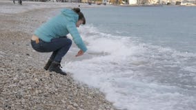 Kobieta przy osamotnioną zimno plażą Kaukaska kobieta odbija się z nadchodzącej fali bawić się z kamieniami blisko wody na zbiory wideo Kobieta przy osamotnioną zimno plażą Kaukaska kobieta odbija się z nadchodzącej fali bawić się z kamieniami blisko wody na zbiory wideo