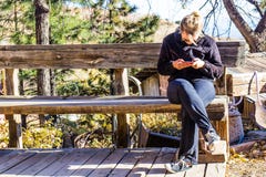 Kobieta Texting Na telefonie komórkowym Na Nieociosanej Drewnianej ławce fotografia stock Kobieta Texting Na telefonie komórkowym Na Nieociosanej Drewnianej ławce fotografia stock