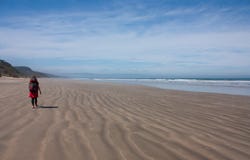 Kobieta wycieczkowicza odprowadzenie na plaży z jej plecakiem przy Humpridge śladem w Fiordland, Southland w Południowej wyspie w zdjęcia royalty free Kobieta wycieczkowicza odprowadzenie na plaży z jej plecakiem przy Humpridge śladem w Fiordland, Southland w Południowej wyspie w zdjęcia royalty free