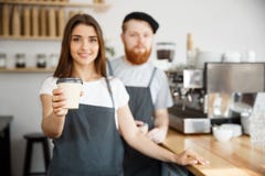 Koffie Bedrijfsconcept - de Positieve jonge gebaarde mens en het mooie aantrekkelijke het paar van damebarista geven halen kop we Stock Afbeeldingen Koffie Bedrijfsconcept - de Positieve jonge gebaarde mens en het mooie aantrekkelijke het paar van damebarista geven halen kop we Stock Afbeeldingen