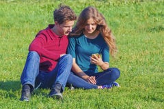 Koppla ihop tonåringar som sitter på den gröna gräsmattan med en smartphone arkivfoto Koppla ihop tonåringar som sitter på den gröna gräsmattan med en smartphone arkivfoto