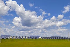 Kraftverksolpaneler på ett grönt fält under en blå himmel med fluffiga moln royaltyfri bild Kraftverksolpaneler på ett grönt fält under en blå himmel med fluffiga moln royaltyfri bild