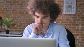 Kranker nerdy Büroangestellter, der an dem Laptop, sitzend im modernen Büro mit Backsteinmauerhintergrund hustet und arbeitet stock footage Kranker nerdy Büroangestellter, der an dem Laptop, sitzend im modernen Büro mit Backsteinmauerhintergrund hustet und arbeitet stock footage