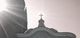 Kreuzen Sie auf die Oberseite der Kapelle im Kirchhof mit Sonnenstrahlen stockbild Kreuzen Sie auf die Oberseite der Kapelle im Kirchhof mit Sonnenstrahlen stockbild