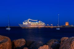 Kryssningskepp på port mellan skymning för två segla yachter royaltyfria foton Kryssningskepp på port mellan skymning för två segla yachter royaltyfria foton