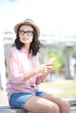 Kvinna som ser bort medan hållande mobiltelefon på bänk utomhus royaltyfria bilder Kvinna som ser bort medan hållande mobiltelefon på bänk utomhus royaltyfria bilder