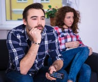 Kvinna som är borrad hållande ögonen på tv med pojkvännen arkivbild Kvinna som är borrad hållande ögonen på tv med pojkvännen arkivbild