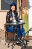 Kvinnasammanträde på en tabell på gatan och drickakaffet royaltyfri bild Kvinnasammanträde på en tabell på gatan och drickakaffet royaltyfri bild