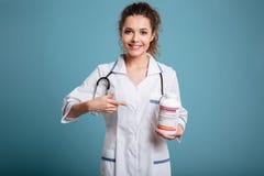 Kvinnlig doktorsinnehavflaska av preventivpillerar och att peka på henne royaltyfri foto Kvinnlig doktorsinnehavflaska av preventivpillerar och att peka på henne royaltyfri foto
