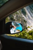 Kvinnlig hand som avspeglas i spegeln för bilsidosikt Den blå medelhavet och vit vaggar i bakgrund arkivbild Kvinnlig hand som avspeglas i spegeln för bilsidosikt Den blå medelhavet och vit vaggar i bakgrund arkivbild