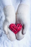 Kvinnlighänder i vit stack tumvanten med flätad ihop romantisk röd hjärta för tappning på snöbakgrund Förälskelse- och St-valenti royaltyfria bilder Kvinnlighänder i vit stack tumvanten med flätad ihop romantisk röd hjärta för tappning på snöbakgrund Förälskelse- och St-valenti royaltyfria bilder