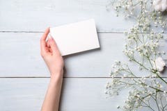 Kvinnors tomt pappers- kort för handinnehav på ljust - blå träbakgrund Lantlig tabell med blommor som gifta sig inbjudankortet, b royaltyfri bild Kvinnors tomt pappers- kort för handinnehav på ljust - blå träbakgrund Lantlig tabell med blommor som gifta sig inbjudankortet, b royaltyfri bild