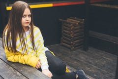 L'adolescente dans le chandail jaune et des jeans noirs s'assied sur une structure en bois photo libre de droits L'adolescente dans le chandail jaune et des jeans noirs s'assied sur une structure en bois photo libre de droits