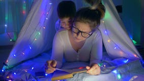L'atmosfera della famiglia, madre preoccupantesi legge le fiabe per scherzare la menzogne nel tepee con le ghirlande a stanza stock footage L'atmosfera della famiglia, madre preoccupantesi legge le fiabe per scherzare la menzogne nel tepee con le ghirlande a stanza stock footage