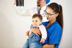 L'enfant contenté dans les bras d'un docteur, à l'arrière-plan le docteur regarde un rayon X Fond blanc image stock L'enfant contenté dans les bras d'un docteur, à l'arrière-plan le docteur regarde un rayon X Fond blanc image stock