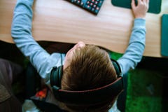 L'enfant s'assied à l'ordinateur et joue des jeux d'ordinateur dans les écouteurs Vue supérieure de la main tenant la souris et l image stock L'enfant s'assied à l'ordinateur et joue des jeux d'ordinateur dans les écouteurs Vue supérieure de la main tenant la souris et l image stock