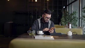 L'homme bel de hippie dactylographie sur l'écran du smartphone se reposant dans le restaurant pendant la journée, comprimé dans l banque de vidéos L'homme bel de hippie dactylographie sur l'écran du smartphone se reposant dans le restaurant pendant la journée, comprimé dans l banque de vidéos