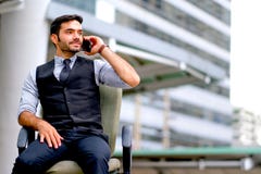 L'homme blanc d'affaires s'assied à la chaise et au téléphone portable d'utilisation pour appeler parmi la ville pendant le temps images stock L'homme blanc d'affaires s'assied à la chaise et au téléphone portable d'utilisation pour appeler parmi la ville pendant le temps images stock