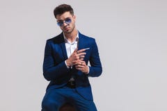 L'homme d'affaires dramatique de mode s'assied et joue avec ses mains photographie stock L'homme d'affaires dramatique de mode s'assied et joue avec ses mains photographie stock
