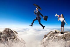 L'homme d'affaires sautant par-dessus une falaise et un coll?gue encourage avec le corne de brume image stock L'homme d'affaires sautant par-dessus une falaise et un coll?gue encourage avec le corne de brume image stock