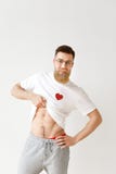 L'homme musculaire bel soulève son T-shirt blanc, démontre le corps nu, pose sur le fond blanc de studio positif photographie stock L'homme musculaire bel soulève son T-shirt blanc, démontre le corps nu, pose sur le fond blanc de studio positif photographie stock