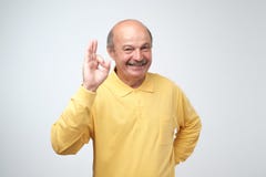 L'homme mûr bel dans le T-shirt jaune montre le signe correct, regardant l'appareil-photo et le sourire images stock L'homme mûr bel dans le T-shirt jaune montre le signe correct, regardant l'appareil-photo et le sourire images stock