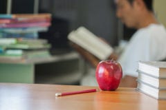 L'image orientée d'école comportant une pomme et une pile des livres le fond est un homme s'asseyant lisant un livre photographie stock libre de droits L'image orientée d'école comportant une pomme et une pile des livres le fond est un homme s'asseyant lisant un livre photographie stock libre de droits