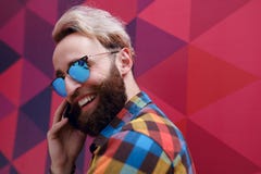 L'immagine di un giovane felice in occhiali da sole, tenente un telefono cellulare, su un fondo variopinto con gli esagoni si for immagini stock libere da diritti L'immagine di un giovane felice in occhiali da sole, tenente un telefono cellulare, su un fondo variopinto con gli esagoni si for immagini stock libere da diritti