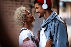 L'uomo afroamericano felice nei heaphones ed il suo buio hanno pelato la femmina con il supporto riccio vicino ad a vicenda, sgua immagine stock L'uomo afroamericano felice nei heaphones ed il suo buio hanno pelato la femmina con il supporto riccio vicino ad a vicenda, sgua immagine stock
