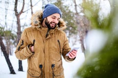 L'uomo barbuto sorridente indossa i vestiti caldi ed utilizzare dell'inverno lo smartphone con la connessione dati veloce di Inte fotografia stock L'uomo barbuto sorridente indossa i vestiti caldi ed utilizzare dell'inverno lo smartphone con la connessione dati veloce di Inte fotografia stock