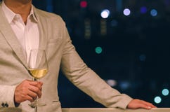 L'uomo d'affari che indossa il vestito grigio di colore sta alla barra del tetto che tiene un vetro di vino bianco con fondo scur fotografia stock L'uomo d'affari che indossa il vestito grigio di colore sta alla barra del tetto che tiene un vetro di vino bianco con fondo scur fotografia stock
