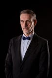 L'uomo d'affari più anziano in un vestito con un farfallino su fondo nero immagini stock L'uomo d'affari più anziano in un vestito con un farfallino su fondo nero immagini stock