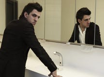L'uomo inutile di affari che controlla suo osserva nello specchio fotografia stock L'uomo inutile di affari che controlla suo osserva nello specchio fotografia stock