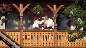 L'uomo, la donna ed il bambino con i vestiti tradizionali al balcone di legno della casa, parents baciare il bambino, ritratto de stock footage L'uomo, la donna ed il bambino con i vestiti tradizionali al balcone di legno della casa, parents baciare il bambino, ritratto de stock footage
