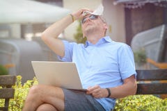 L'uomo soffre dal calore mentre lavora con il computer portatile fotografia stock L'uomo soffre dal calore mentre lavora con il computer portatile fotografia stock