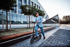 L'uomo sta conducendo il suo nuovo elettro motorino vicino a grande costruzione di vetro immagine stock libera da diritti L'uomo sta conducendo il suo nuovo elettro motorino vicino a grande costruzione di vetro immagine stock libera da diritti