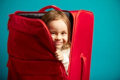 La bambina guarda dalla valigia rossa su fondo isolato blu immagine stock La bambina guarda dalla valigia rossa su fondo isolato blu immagine stock