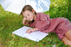 La bambina sveglia insegna alle lezioni nella natura nel parco il bambino legge il libro immagini stock libere da diritti La bambina sveglia insegna alle lezioni nella natura nel parco il bambino legge il libro immagini stock libere da diritti